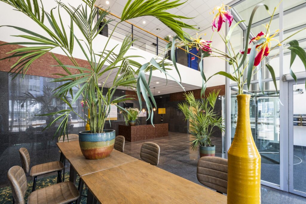 Modern office lobby at Bos en Lommerplein with large indoor plants, wooden furniture, and a bright, open atmosphere.